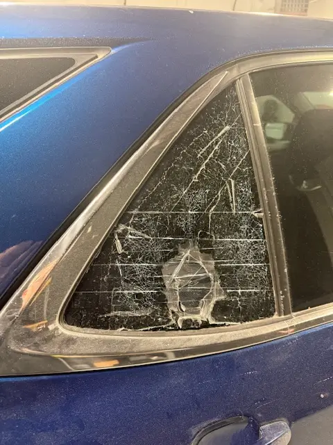 A car door glass shattered with shards on the seats.